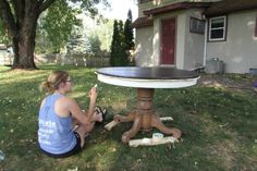 a woman sitting on the ground next to a table in front of a house with candles around it