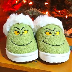 a pair of green slippers with yellow eyes and fluffy white hair on top of a wooden table