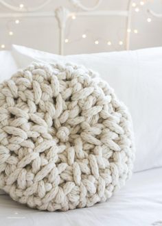 a white knitted pillow sitting on top of a bed