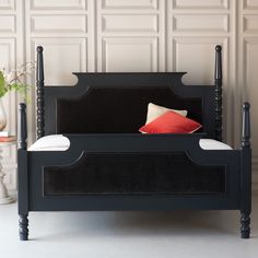 a black bed frame with red pillows on it and white walls in the back ground