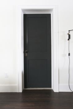 an empty room with a black door and white walls, wood flooring is in the foreground