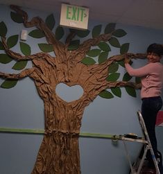 a woman standing on a ladder in front of a tree with the word exit painted on it