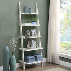 a white leaning shelf with books and vases on the floor in front of a green wall