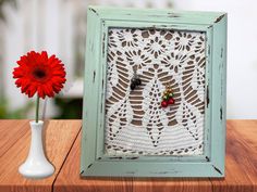 a red flower sitting next to a small white vase with a crochet doily on it