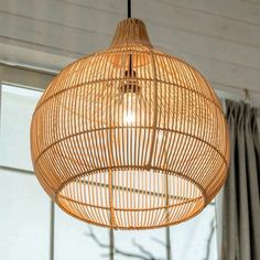 a bamboo light hanging from the ceiling in a living room with curtains and windows behind it