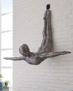 a sculpture of a person hanging from the side of a white brick wall in front of a window