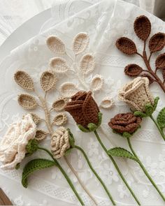 four crocheted flowers on a white doily with green stems and leaves in the middle