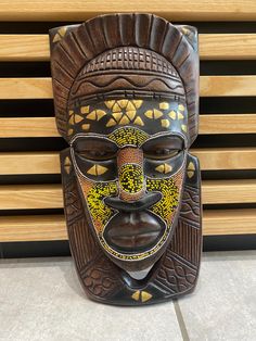 a wooden mask sitting on top of a tile floor next to a wood slatted wall