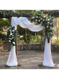 an outdoor wedding arch decorated with white and pink flowers, greenery and draping