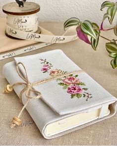 a white book with flowers on it sitting next to some tape and a potted plant