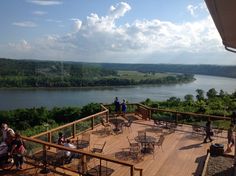 people sitting at tables on a deck overlooking the water