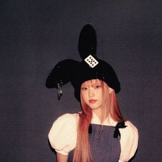 a woman with long red hair wearing a black hat and blue overalls is posing for the camera