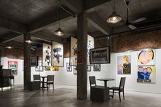 an empty room with paintings on the wall and tables in the center, surrounded by chairs