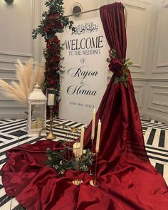 a red wedding dress on display in front of a welcome sign with candles and greenery