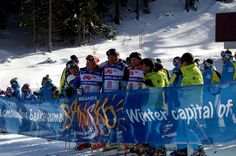 a group of people standing behind a banner on top of a snow covered ski slope