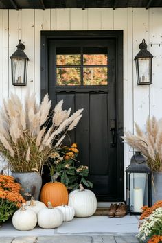 a front door with pumpkins and flowers on the steps next to it is lit by lanterns