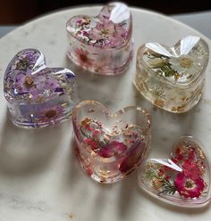 four heart shaped glass boxes sitting on top of a white table with flowers in them