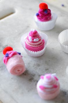 small cupcakes with pink frosting and red decorations on a marble slab top