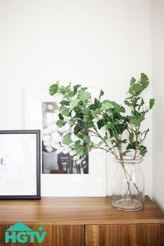 a vase filled with green leaves sitting on top of a wooden table next to a framed photo