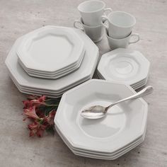 a table set with plates, cups and spoons on top of each other next to a red flower