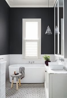 a white bath tub sitting under a bathroom window next to a sink and shower stall