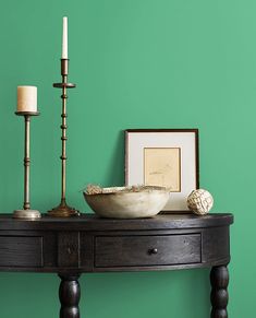 a wooden table topped with a bowl next to a candle and framed pictures on the wall