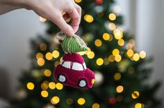 a hand holding a knitted ornament with a car on it and a christmas tree in the background