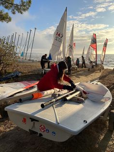 a person in a red jacket and some sailboats on the beach with people standing around