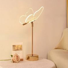 a table with a lamp on top of it next to a white couch and pink rose