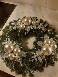 a christmas wreath with silver and white ornaments on top of a marble counter next to a stove