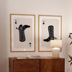 two framed pictures on the wall above a dresser with a lamp and vase in front of them