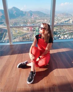 a woman sitting on top of a wooden floor in front of a window looking out at the city