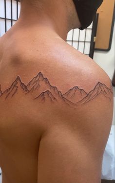 the back of a man's shoulder with mountains tattoo on his left arm and chest