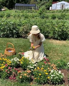 a woman kneeling down in the middle of a flower garden with a basket and flowers