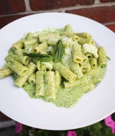 a white plate topped with pasta covered in pesto sauce and green leafy garnish