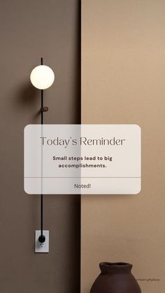 a brown vase sitting on top of a table next to a wall mounted light with the words today's reminder