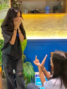 two women sitting down and one is covering her mouth while the other holds her hands up