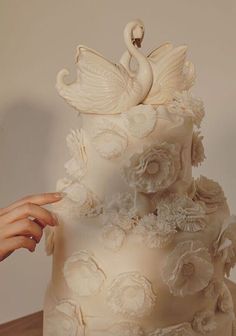 a woman is holding up a wedding cake decorated with flowers and swan figurines