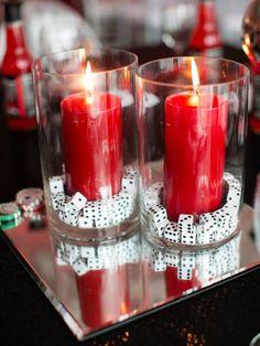 two red candles are sitting in glass cups on a table with silverware and other decorations