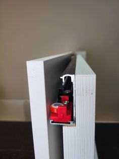 a red and black object is in the corner of a white box with a door open