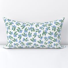 a white pillow with blue flowers and green leaves on the front is sitting on a table