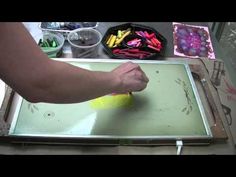 a person is using a yellow sponge to paint on a piece of paper with colored crayons in the background