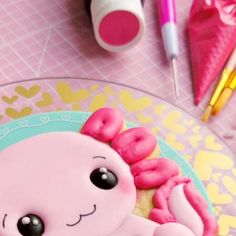 a pink octopus cake sitting on top of a plate next to markers and pencils