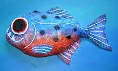 a blue and red fish with black dots on it's eyes, sitting on a blue surface