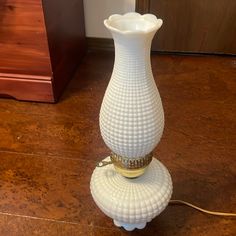 a white vase sitting on top of a wooden floor next to a lamp shade holder