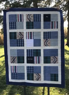 a blue and white quilt is hanging on a stand in the grass next to some trees