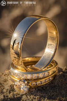 two wedding rings sitting on top of each other in the sand with their reflection in them