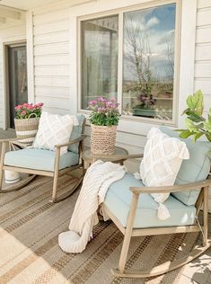 two chairs and a table on a porch with potted plants in front of the window