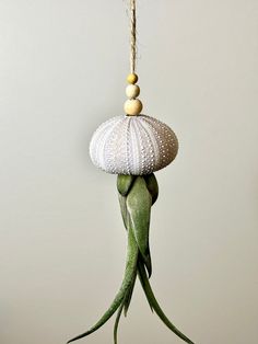 a green and white bird hanging from a string with beads on it's head