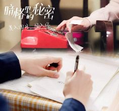 two people sitting at a table writing on paper and using a red typewriter in front of them